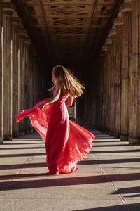 Full length rear view of young woman in pink evening gown dancing at colonnade