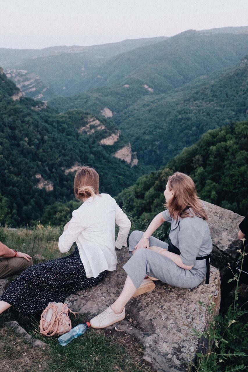 sitting, mountain, women, adult, leisure activity, two people, togetherness, nature, plant, full length, relaxation, men, tree, landscape, female, lifestyles, casual clothing, environment, scenics - nature, mountain range, land, emotion, friendship, day, holiday, beauty in nature, forest, tranquility, vacation, trip, happiness, young adult, bonding, adventure, outdoors, positive emotion, smiling, non-urban scene, sky, activity, high angle view, love, food and drink, tranquil scene, travel, enjoyment, rural scene, resting, grass, child, family, simple living, person, summer, communication, clothing, recreation, blond hair, childhood