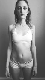 Portrait of woman wearing sports bra while standing against wall