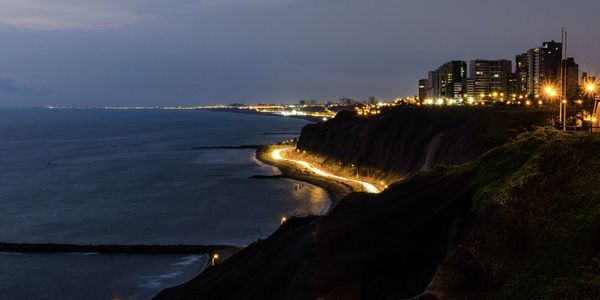 Illuminated buildings by sea against sky at night