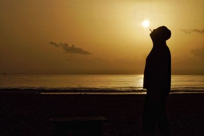 Silhouette man standing on beach against sky during sunset