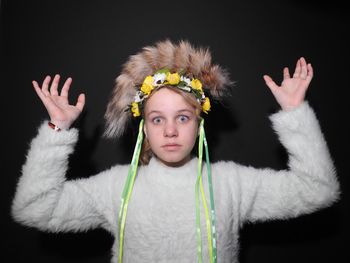 Portrait of shocked girl with arms raised wearing warm clothing against black background