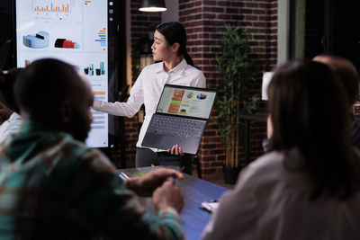 Businesswoman holding laptop explaining graph in office