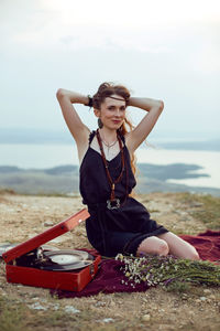 Young woman lies in nature in a black dress next to an old gramophone and listens to music
