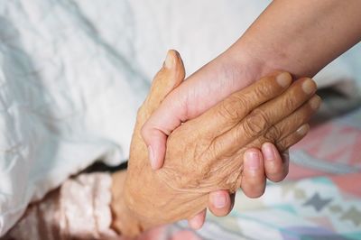 Cropped image of person holding senior woman hand at home