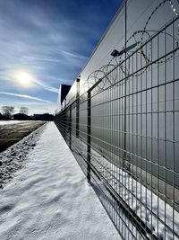 Snow covered fence against sky during winter