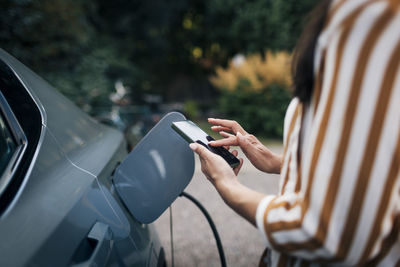 Midsection of mature woman using smart phone while charging car in back yard
