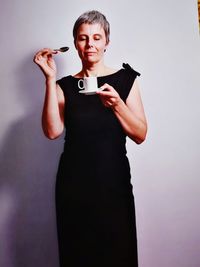 Mature woman holding coffee cup while standing against wall