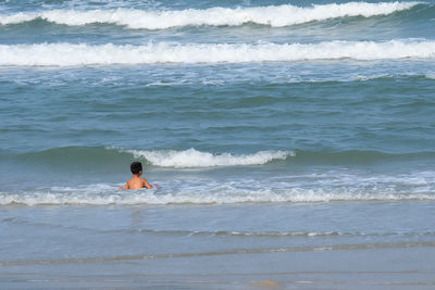 Rear view of shirtless boy swimming at beach
