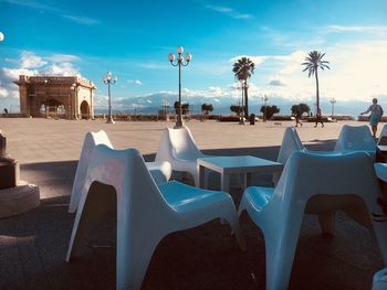 Empty chairs and tables by swimming pool against sky