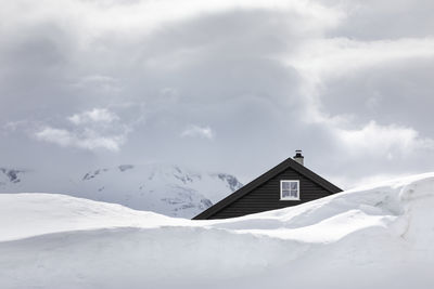 Roof and gable window from a wooden house hidden behind huge snow wall high up in the mountains