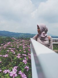 Smiling young woman in hijab standing by railing against sky
