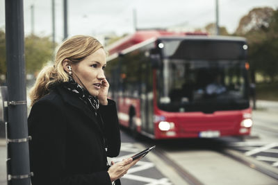 Side view of businesswoman talking on mobile phone with bus in background