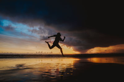 Silhouette man jumping on beach against sky during sunset