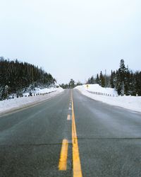 Road by trees against sky during winter