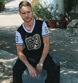 Portrait of young man sitting on seat at footpath