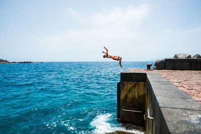 Man jumping on sea against sky