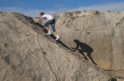 Man climbing on rock against sky