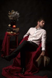 Young man sitting against red background