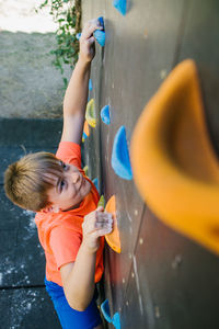 Side view of unrecognizable fearless child balancing on grips and climbing wall while practicing bouldering in gym