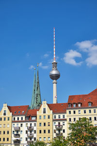 Tower amidst buildings in city against blue sky