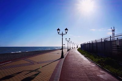 Row of gas lights on promenade by sea against blue sky