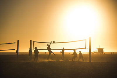 Silhouette people playing beach volleyball on land against sky during sunset