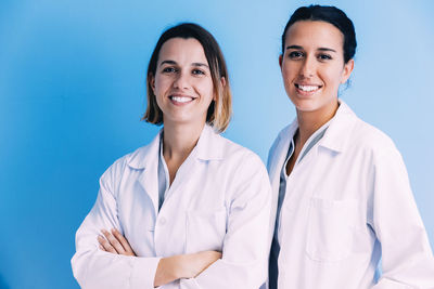 Portrait of smiling doctors with arms crossed standing against wall