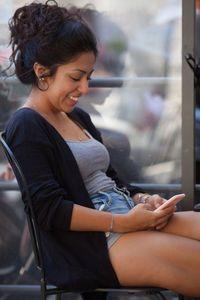 Side view of young woman sitting on window