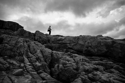 Low angle view of man standing on cliff against cloudy sky