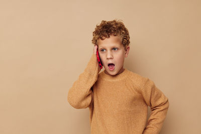 Boy talking on phone against beige backgrounds