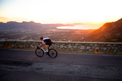 Man riding bicycle on mountain against sky during sunset