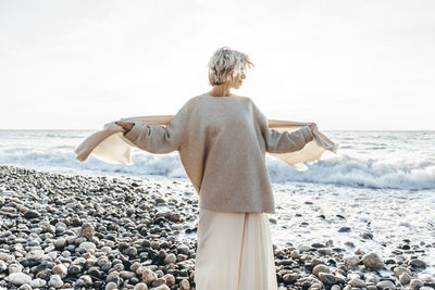 Woman holding blanket standing on stones at beach