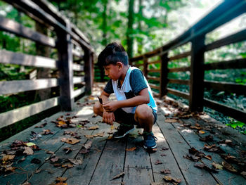 Full length of boy crouching on footbridge during autumn