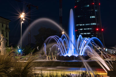 Illuminated light trails over fountain in city at night