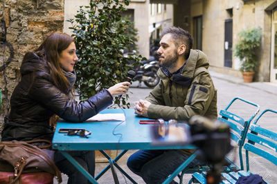 The woman holds a microphone to interview a man near him