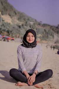 Portrait of young woman wearing hijab sitting at beach