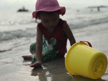 Girl holding bucket while sitting at beach