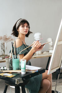 Side view portrait of confident woman holding paintbrush and palette at art studio