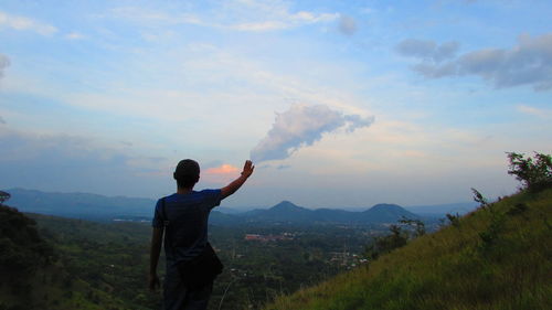 Optical illusion of man touching cloud in sky