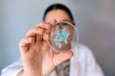 Portrait of female scientist looking blue glitter sample over petri dish on laboratory