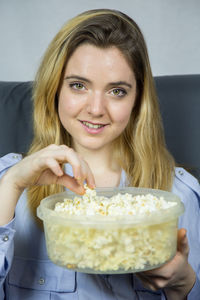 Portrait of young woman having popcorn while sitting on sofa at home