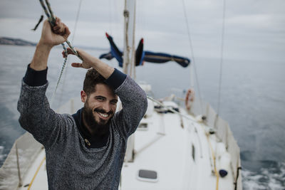 Smiling young man holding rope of sailboat in mediterranean sea