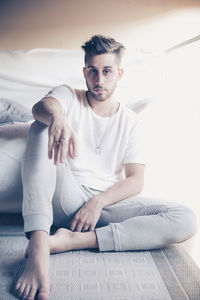 Portrait of man sitting by bed at home