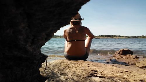 Rear view of young woman in bikini sitting on rock at beach