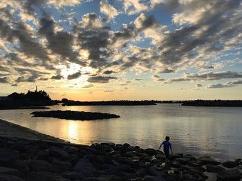 Silhouette woman standing by lake against sky during sunset