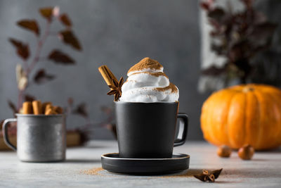 Pumpkin latte with whipped cream and a stick of cinnamon in a mug.