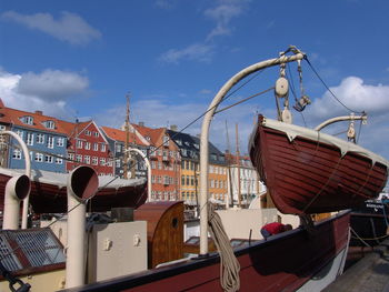 Boats moored at harbor by buildings against sky