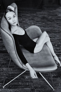 A ballerina in a bodysuit and pointes is sitting on a sofa in a loft with her hands behind her head