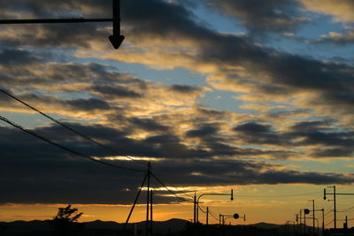 Low angle view of silhouette electricity pylon against dramatic sky during sunset